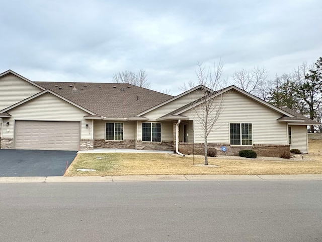 ranch-style home with brick siding, an attached garage, a front lawn, roof with shingles, and driveway