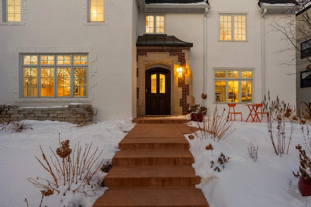 snow covered property entrance featuring a standing seam roof, metal roof, and stucco siding