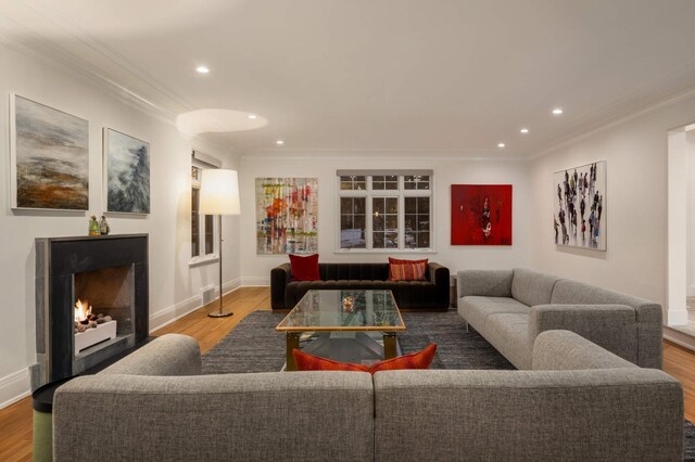 living room featuring a warm lit fireplace, crown molding, wood finished floors, and recessed lighting