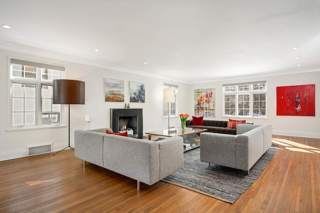 living room with a warm lit fireplace, ornamental molding, wood finished floors, and visible vents