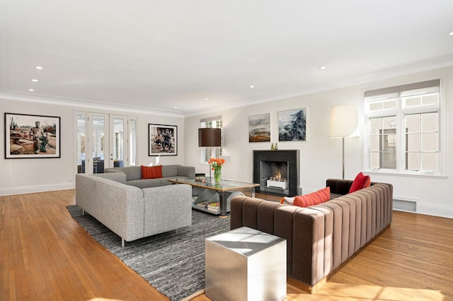 living area with light wood-style floors, french doors, crown molding, and a lit fireplace