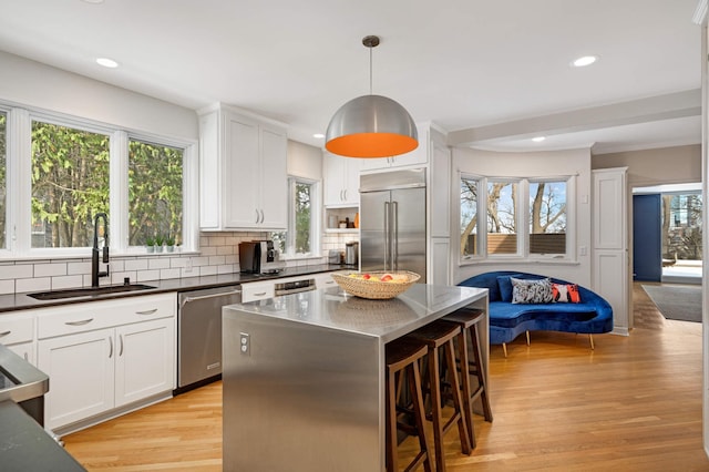 kitchen with a center island, a breakfast bar, stainless steel appliances, dark countertops, and a sink