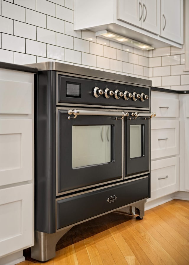 kitchen featuring dark countertops, light wood finished floors, white cabinets, and backsplash