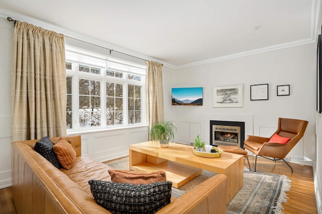 sitting room with crown molding, a lit fireplace, a decorative wall, and wood finished floors