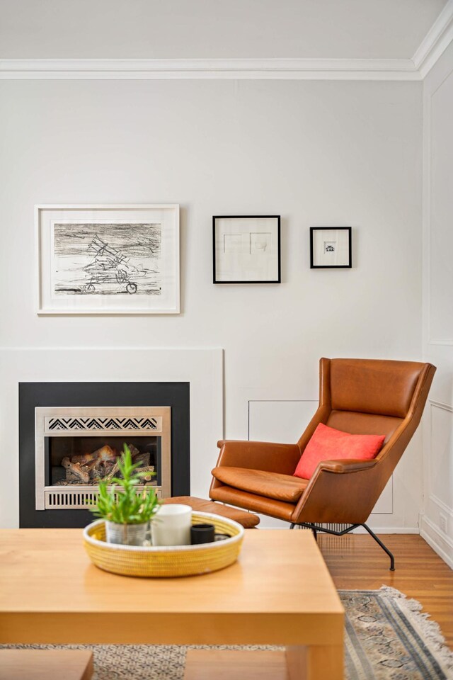 sitting room featuring a fireplace, wood finished floors, and crown molding