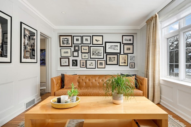 sitting room with visible vents, ornamental molding, a decorative wall, and wood finished floors