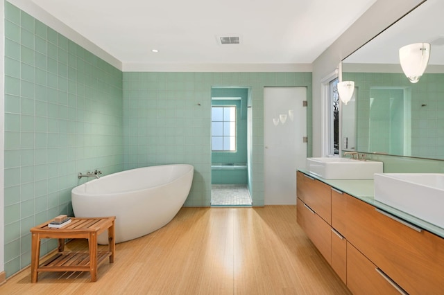 bathroom featuring tile walls, a soaking tub, visible vents, a sink, and wood finished floors