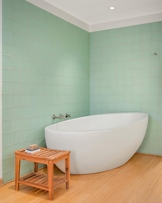 bathroom with a soaking tub, tile walls, and wood finished floors