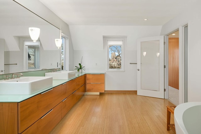 bathroom featuring a soaking tub, double vanity, a sink, and wood finished floors