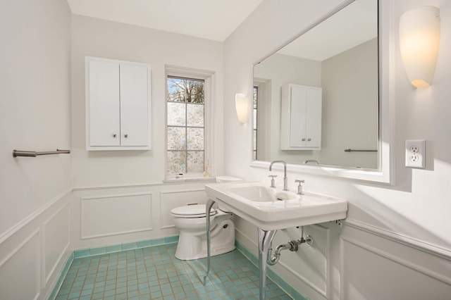 half bathroom featuring tile patterned flooring, a wainscoted wall, a decorative wall, and toilet