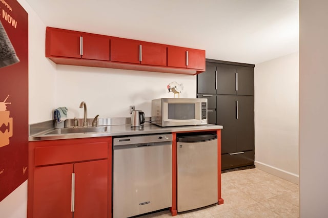 kitchen with red cabinets, stainless steel countertops, appliances with stainless steel finishes, a sink, and baseboards