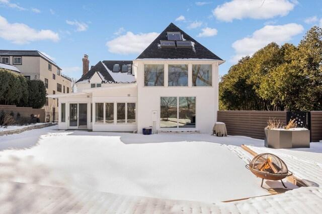 snow covered property with an outdoor fire pit, fence, a sunroom, and stucco siding