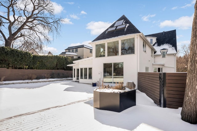 snow covered rear of property featuring fence and stucco siding