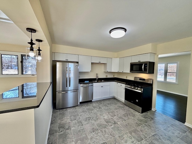 kitchen featuring stainless steel appliances, dark countertops, white cabinetry, a sink, and baseboards