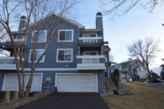 view of front of property with a garage, driveway, a chimney, and a balcony