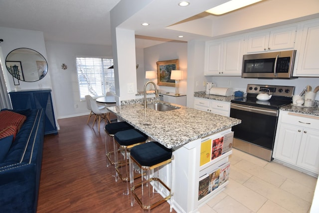 kitchen featuring stainless steel appliances, white cabinetry, a sink, and light stone countertops