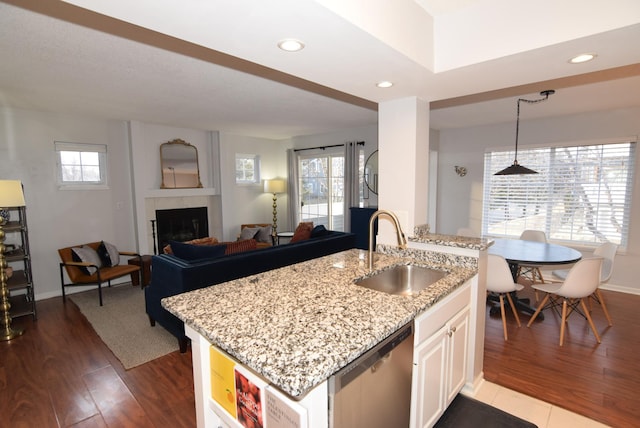 kitchen with dishwasher, a tiled fireplace, open floor plan, wood finished floors, and a sink