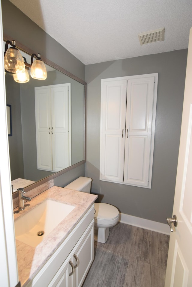 bathroom with toilet, wood finished floors, vanity, visible vents, and baseboards