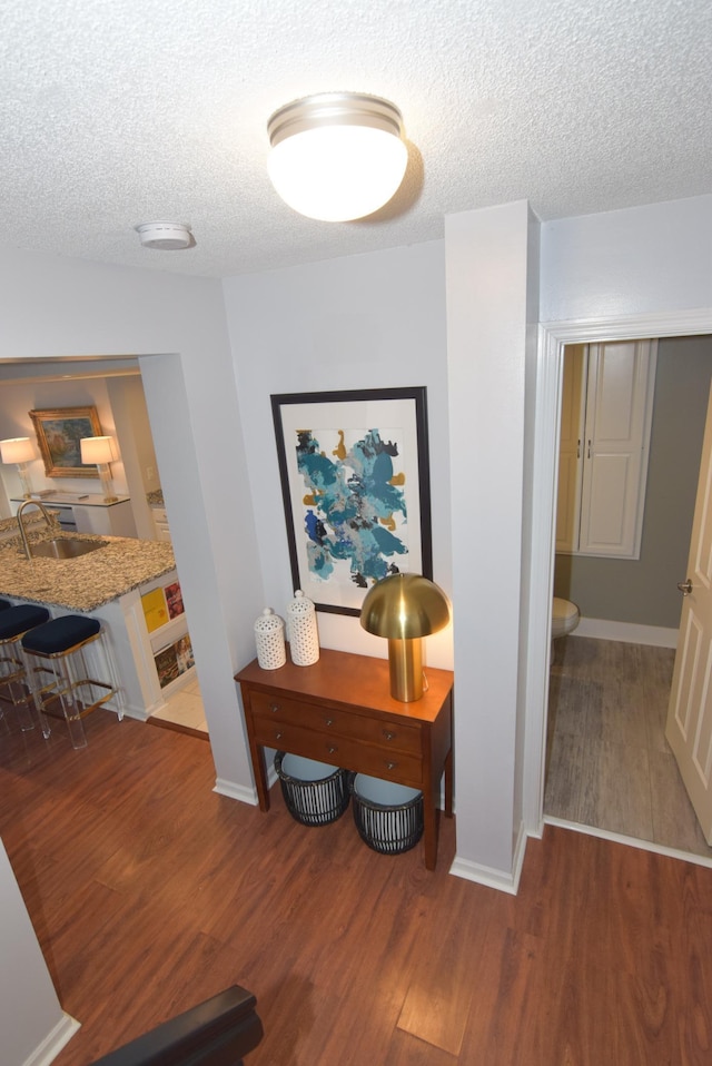 corridor with a sink, a textured ceiling, baseboards, and wood finished floors