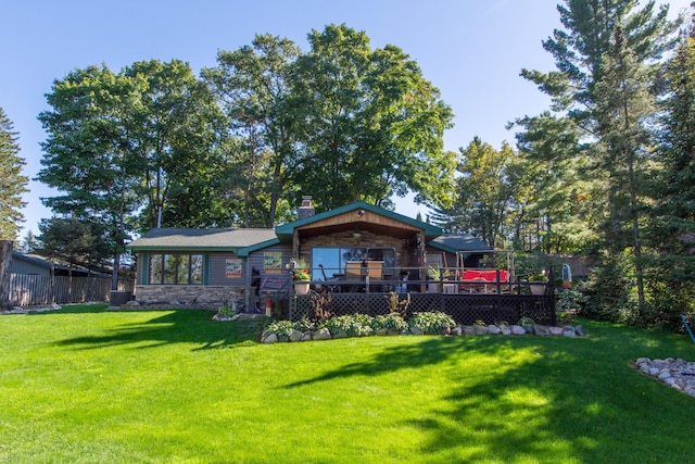 rear view of house with a yard, a chimney, fence, a deck, and stone siding