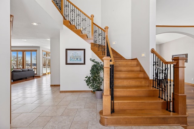 stairway with tile patterned flooring, baseboards, recessed lighting, a towering ceiling, and arched walkways