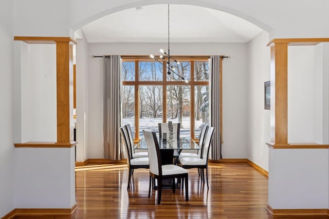 dining room with arched walkways, an inviting chandelier, wood finished floors, and ornate columns