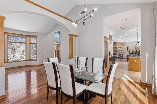 dining space with a stone fireplace, vaulted ceiling, arched walkways, and light wood-type flooring