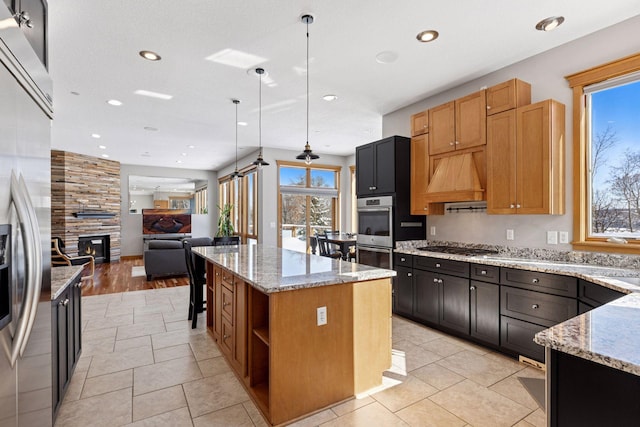 kitchen with a kitchen island, light stone countertops, open floor plan, a fireplace, and stainless steel appliances