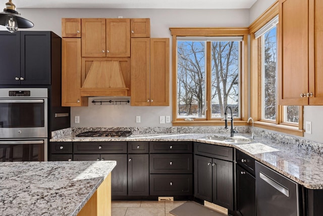 kitchen with light tile patterned floors, light stone countertops, premium range hood, a sink, and stainless steel appliances