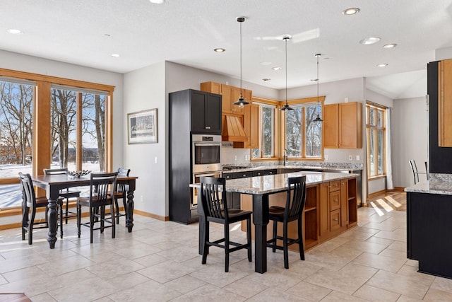 kitchen with a kitchen bar, pendant lighting, a center island, baseboards, and light stone countertops