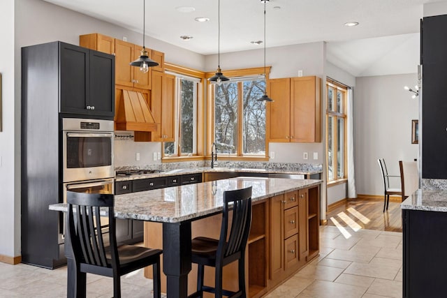 kitchen with a center island, premium range hood, decorative light fixtures, light stone counters, and a sink