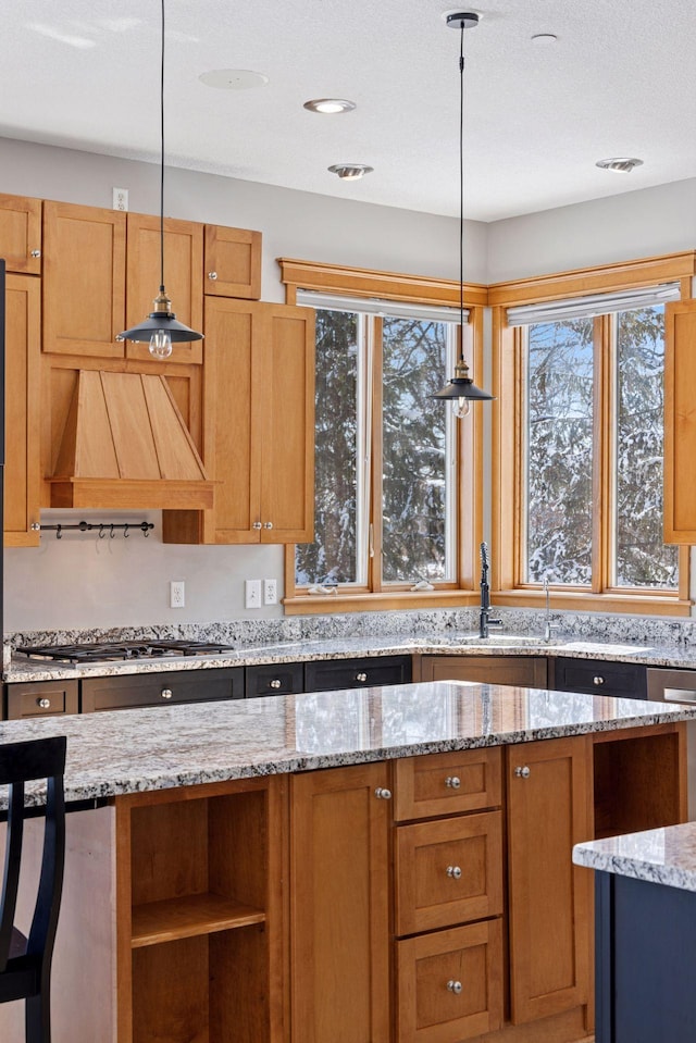 kitchen with light stone countertops, stainless steel gas cooktop, open shelves, custom range hood, and decorative light fixtures