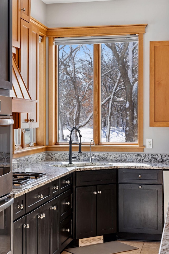 kitchen featuring a sink, stainless steel appliances, dark cabinetry, and light stone countertops