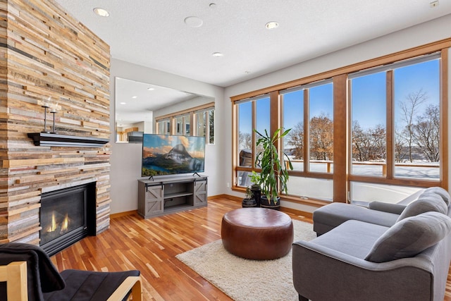 living area featuring a fireplace, a textured ceiling, baseboards, and wood-type flooring