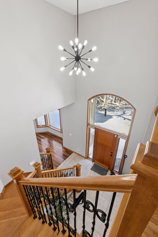 staircase with baseboards, wood finished floors, a high ceiling, and a chandelier