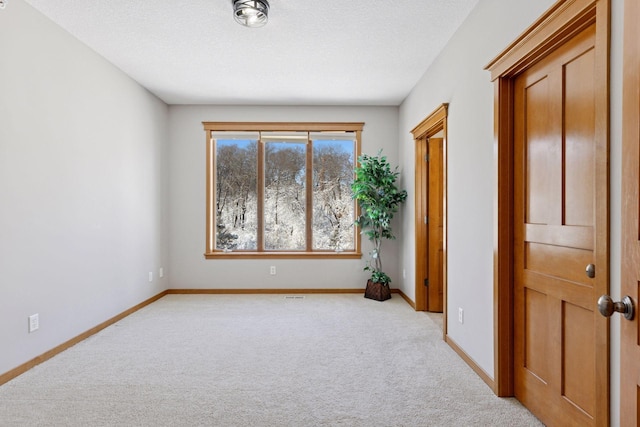 empty room featuring light carpet, a textured ceiling, and baseboards