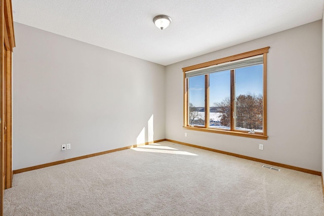 unfurnished room featuring a textured ceiling, carpet, visible vents, and baseboards