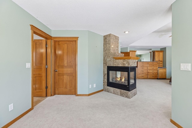 living room with a multi sided fireplace, baseboards, light colored carpet, and a textured ceiling