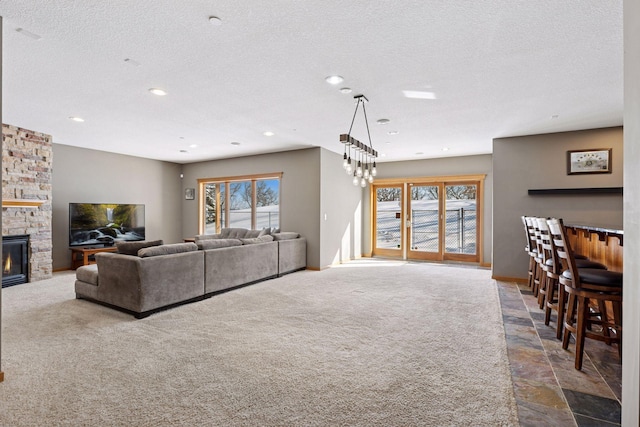 carpeted living room featuring a stone fireplace, a healthy amount of sunlight, and a textured ceiling