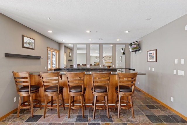 bar with baseboards, wet bar, and stone finish floor