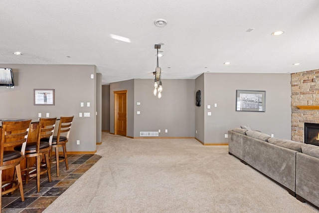 carpeted living room with baseboards, visible vents, a stone fireplace, and a bar