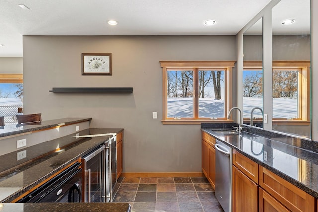 kitchen with baseboards, wine cooler, stone tile floors, brown cabinets, and a sink