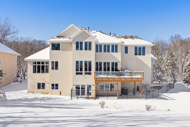 snow covered house with fence and stucco siding