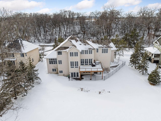 snow covered rear of property with a deck, fence, and stucco siding