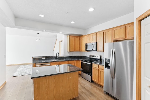 kitchen with a peninsula, a sink, appliances with stainless steel finishes, light wood-type flooring, and a center island