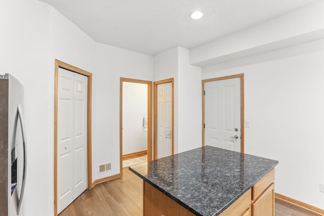 kitchen with stainless steel fridge with ice dispenser, visible vents, a kitchen island, light wood-type flooring, and baseboards