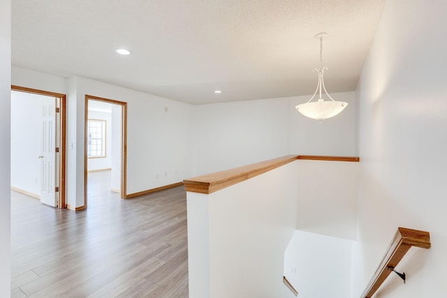 hall featuring light wood-type flooring, recessed lighting, baseboards, and an upstairs landing