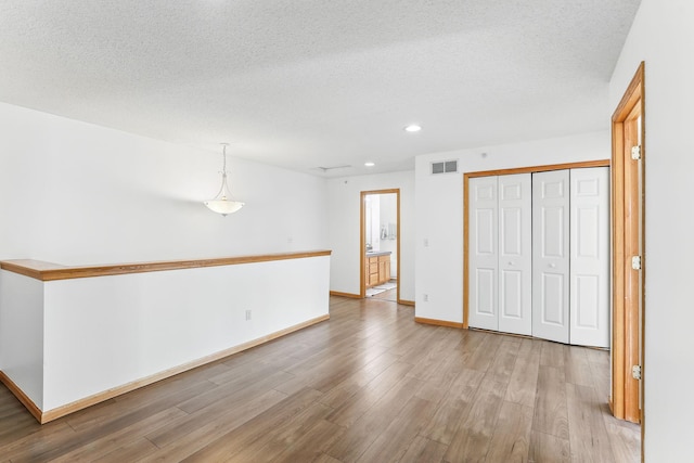 spare room with a textured ceiling, light wood-style flooring, recessed lighting, visible vents, and baseboards