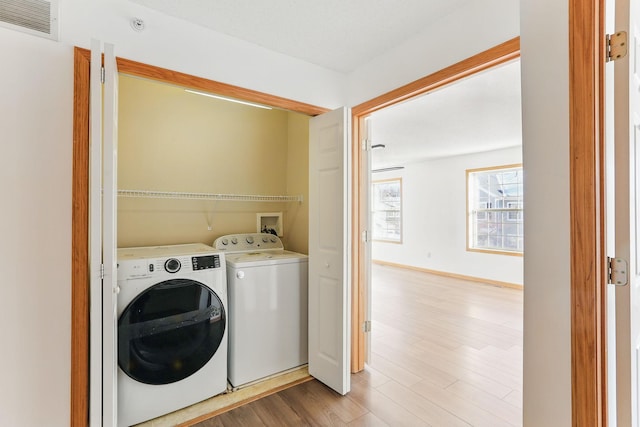 washroom featuring laundry area, visible vents, washer and clothes dryer, baseboards, and light wood-style flooring