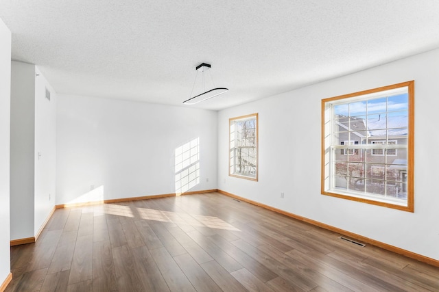 empty room featuring a healthy amount of sunlight, visible vents, and wood finished floors